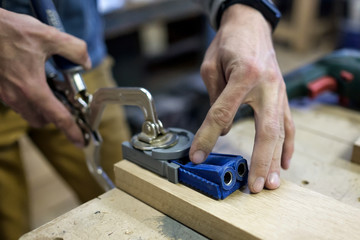 Woodwork and furniture making concept. Caucasain man carpenter installs the furniture hinge. Pocket...
