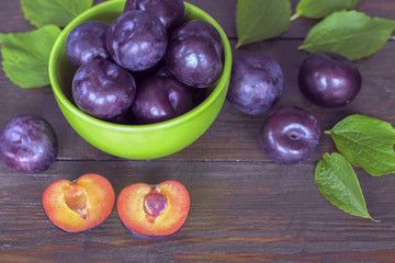 ripe purple plums in a green bowl close-up on a wooden table. plum halves and whole plums close-up.