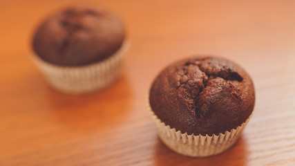 two chocolate muffins on the brown wooden table.