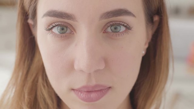 Extreme close-up of a beautiful female face. Pretty Caucasian woman with grey eyes looking at the camera and smiling.
