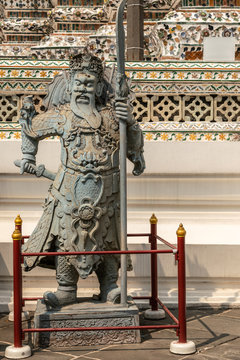 Bangkok city, Thailand - March 17, 2019: Chinese style warrior statue at bottom of Temple of Dawn, with porcelain faience decoration in back.