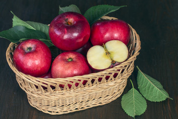 red fresh apples. apples in a wicker basket on a wooden table closeup. background with apples and leaves. crop of apples.