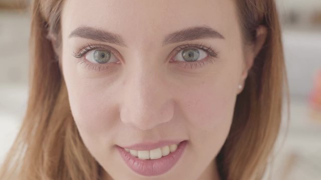 Extreme close-up of a beautiful Caucasian woman with grey eyes looking at the camera and smiling.