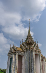 Fototapeta premium Bangkok city, Thailand - March 17, 2019: Facades, Gables and greenish spire of smaller section of Temple of Dawn, with its colorful porcelain faience surface, golden roof, against blue sky.