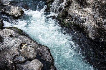 CLOSE UP: Foaming river water flows down large black rocks in the middle of a tropical forest