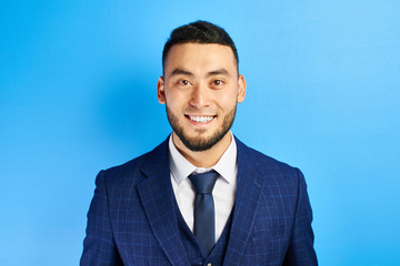 Portrait of smiling handsome successful kazakh asian businessman in suit on blue studio background isolated