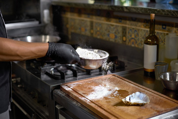 Food concept. The Chef sprinkles flour Fresh Oysters for Roasting in the kitchen. The process of...