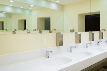 Diagonal view of cutting-edge public toilet room with white ceramic basins and soapbox