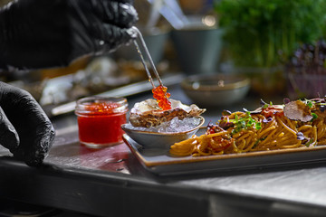 The chef garnishes with red caviar a seafood spaghetti dish. Selective focus.