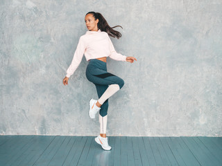 Fototapeta na wymiar Portrait of confident fitness woman in sports clothing looking confident.Young female wearing sportswear. Beautiful model with perfect tanned body.Female jumping in studio near gray wall