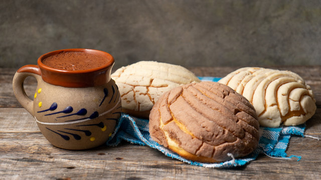 Mexican hot chocolate with sweet conchas bread on wooden background