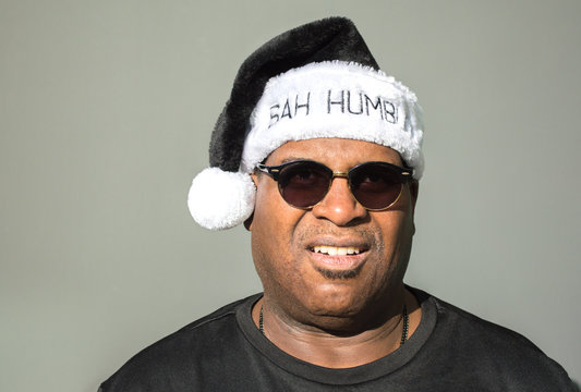 cranky African American man wearing sunglasses and a black and white Bah Humbug hat isolated on a solid background