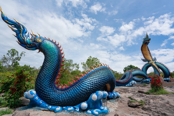Giant Thai Naga Statue with blue sky clouds in the Phu Manorom Temple, Statue of Naka Buddha and White large Buddha statue at Mukdahan Province, Thailand.
