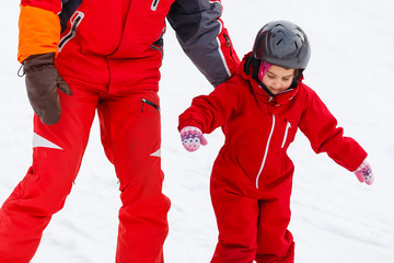 Little girl in red learning to ski with the help of an adult