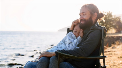 Cute child girl sits on hands of her father and they embracing. Happy family on vacation at lake...