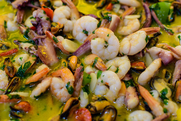 Close up of large portion of traditional Spanish paella dish freshly being cooked with seafood and pasta in a  frying pan at a street food festival, ready to eat seafood, side view, selective focus