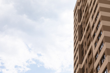 Blue cloudy sky background on one side of photo and high apartment building with beige walls on the right, exterior architecture design - Powered by Adobe