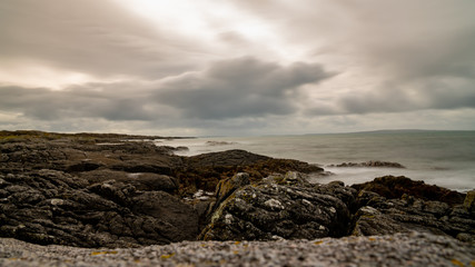 Fototapeta na wymiar Cloudy sky above rocks, silky smooth water and sharp stones, part of Wild Atlantic Way in Ireland. West Coast