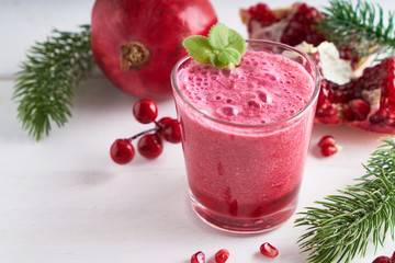 pomegranate smoothie in a glass on a white wooden table with fir branches and winter berries Close-up