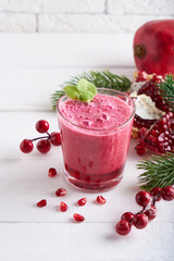 pomegranate smoothie in a glass on a white wooden table with fir branches and winter berries Close up