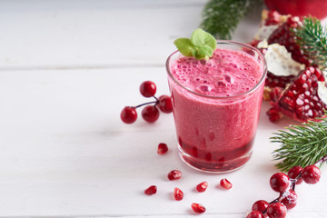pomegranate smoothie in a glass on a white wooden table with fir branches and winter berries Copyspace