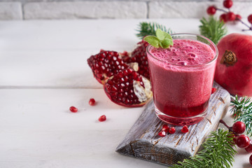 pomegranate smoothie in a glass on a white wooden table with fir branches and winter berries...