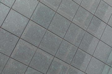 Gray stone square tiles on wall or floor, ground with diagonal view.