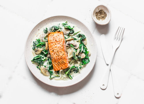 Roasted salmon with creamy spinach mushrooms sauce on a light background, top view. Salmon florentine