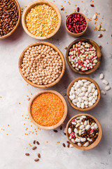 Lentils, chikpea and beans assortment in different bowls on white stone  table top view.