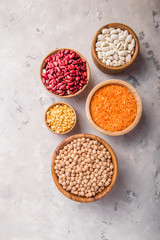Lentils, chikpea and beans assortment in different bowls on white stone  table top view.