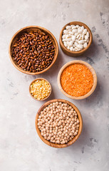 Lentils, chikpea and beans assortment in different bowls on white stone  table top view.