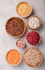 Lentils, chikpea and beans assortment in different bowls on white stone  table top view.