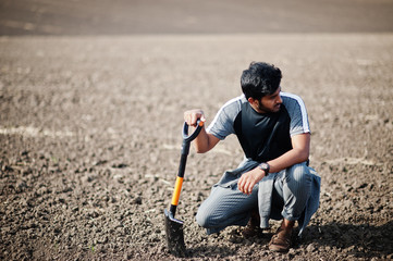 South asian agronomist farmer with shovel inspecting black soil. Agriculture production concept.