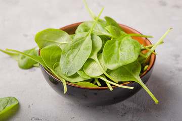 Baby spinach leaves in bowl  on grey concrete background, top view, copy space. Clean eating,...