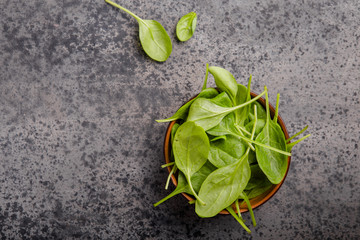 Baby spinach leaves in bowl  on grey concrete background, top view, copy space. Clean eating,...