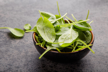 Baby spinach leaves in bowl  on grey concrete background, top view, copy space. Clean eating,...