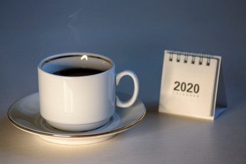 On a white table is a cup of coffee and a desk calendar for 2020.