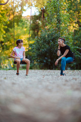 Mother and daughter with a dog sitting on swing and talking