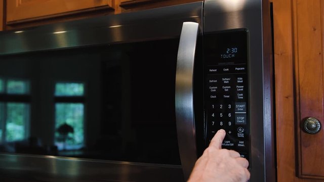 Man programming modern microwave oven. Stainless steel kitchen cooking appliance with digital keypad.