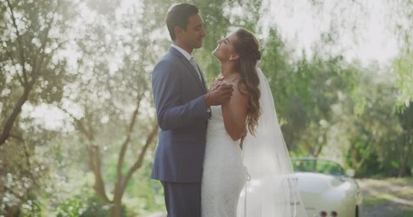 Diverse bride and groom slow dancing in nature outdoors on their wedding day, happy multi ethnic married couple slow dancing in the afternoon sunlight