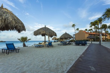 Beautiful view of white sand Aruba beach. Blue sunbeds under sun umbrellas on turquoise water and blue sky with white clouds background. Caribbean. Atlantic ocean. 