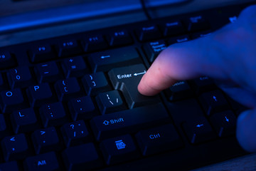 Finger hacker or spy in the dark, presses the enter button on the keyboard.