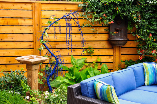 Detail of a relaxing modern urban garden, with horizontal Asian inspired cedar fencing, low maintenance planting, a fountain and bird bath. Comfortable patio furniture adds style.