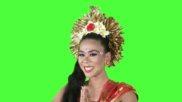 Balinese dancer smiling at the camera while showing a welcoming gesture in the studio. Shot in 4k resolution with green screen background