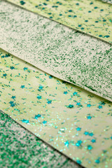 This is a photograph of an abstract background created by organizing stripes created using light and dark Green glitter paint and star sequins