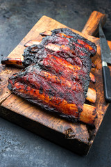 Barbecue burnt chuck beef ribs marinated with hot chili sauce as closeup on an old rustic wooden cutting board