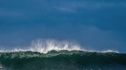 Seascape. Powerful ocean wave on the surface of the ocean. Wave breaks on a shallow bank. Stormy weather, stormy clouds sky background.
