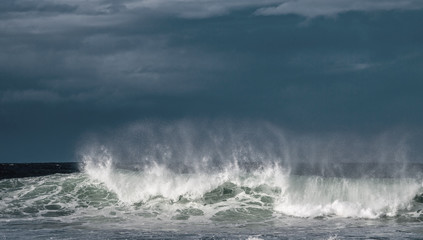 Seascape. Powerful ocean wave on the surface of the ocean. Wave breaks on a shallow bank. Stormy weather, stormy clouds sky background.