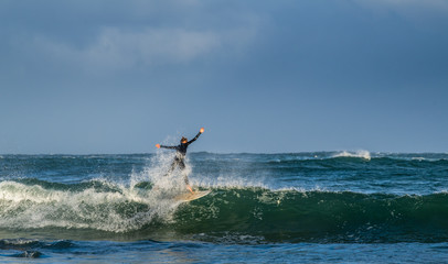 Mossel Bay, South Africa. Surfing the waves. Surfer riding wave with rainbow on storm sky background.