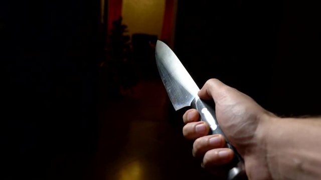 concept of halloween, violence. first-person view. male hand with a knife moves along a dark corridor